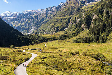 Zwei Radfahrer radeln in trauhafter Bergkulisse und bei bestem Wetter in ein Tal des Nationalparks Hohe Tauern
