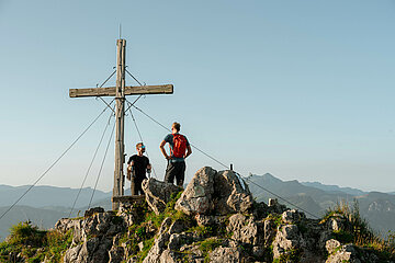 Zwei Gipfelstürmer genießen die wunderbare Aussicht am Gipfelkreuz