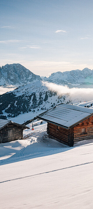 Skiurlaub auf einer Hütte neben der Piste gefällig? Zwei Hütten mitten in den Bergen bei Sonnenschein neben einer Skipiste