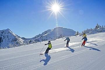 Almliesl Hüttenurlaub in den Bergen buchen Drei Skifahrer wedeln bei herrlichem Winterwetter über eine Piste in Schladming